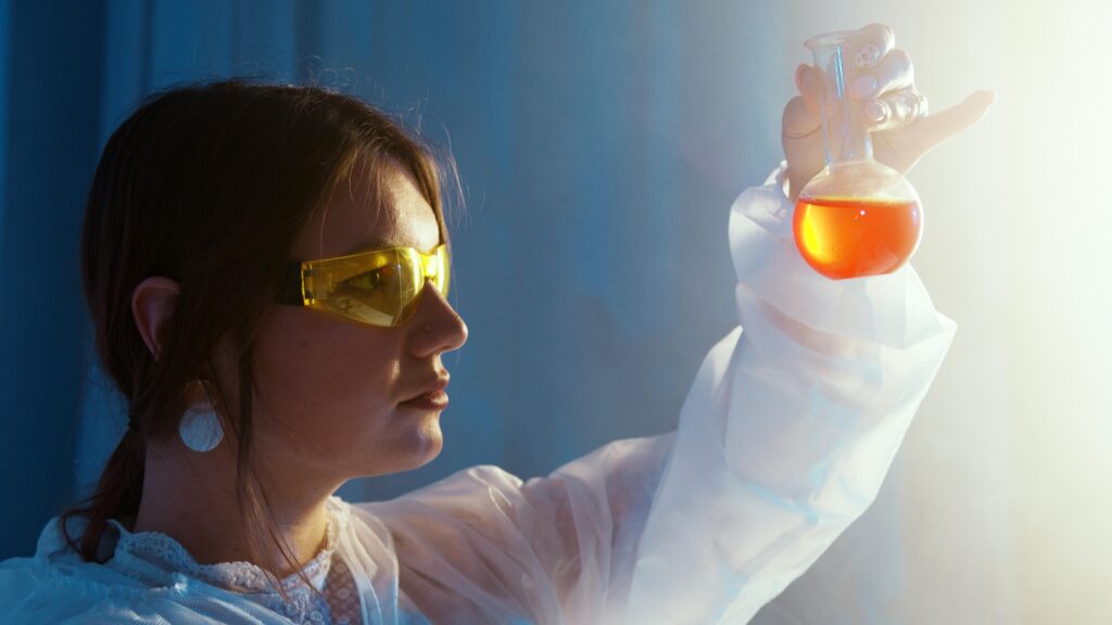 pexels photo 5726788 5726788 Woman in lab coat examining a vibrant liquid in a flask under lab lights.